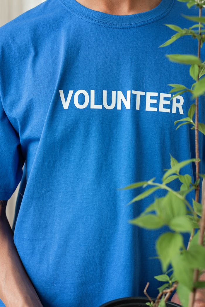 Blue-shirted volunteer with plant, reflecting community work and environmental care.